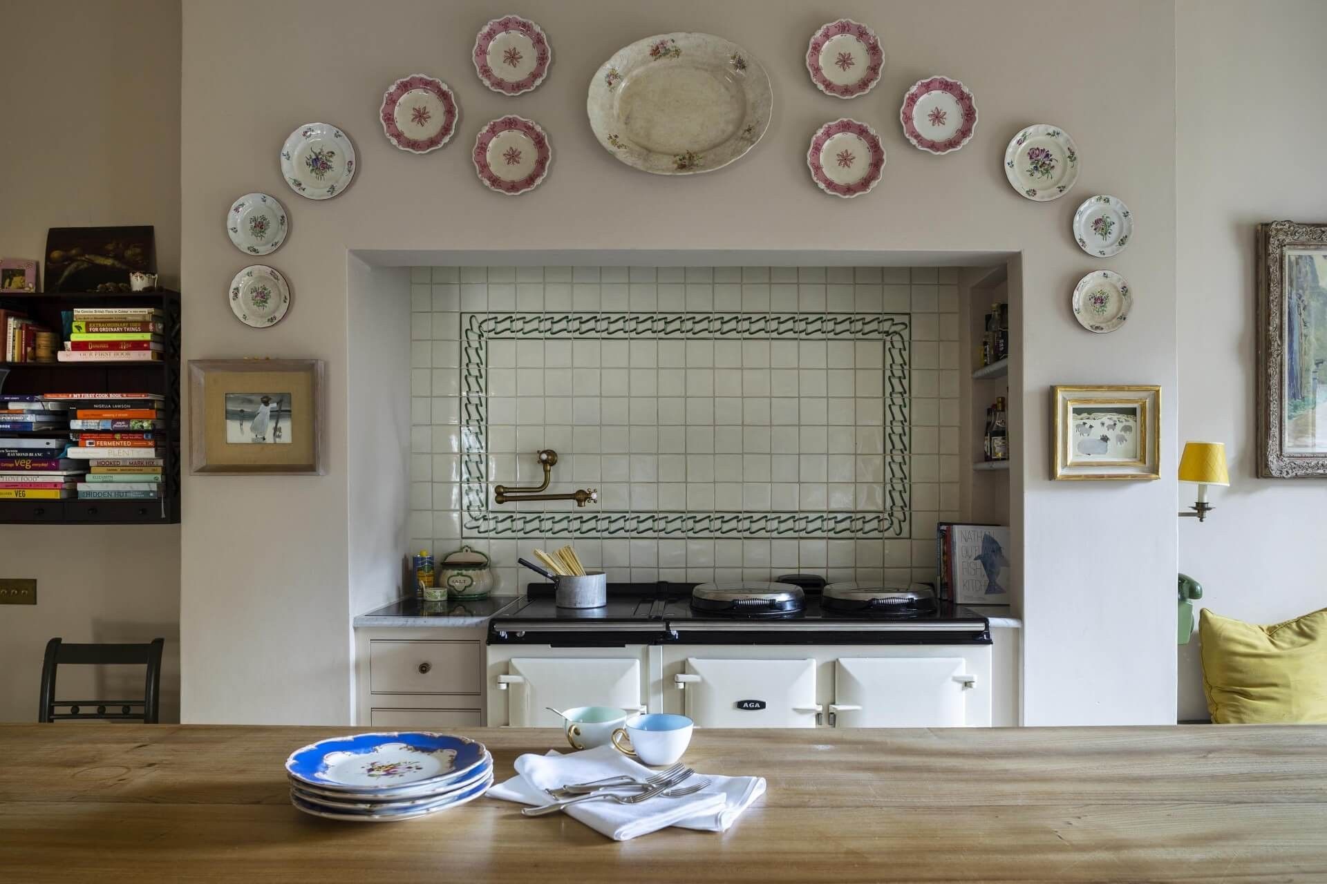 AGA crème encastrée dans une niche carrelée, mur d’assiettes anciennes et table en bois