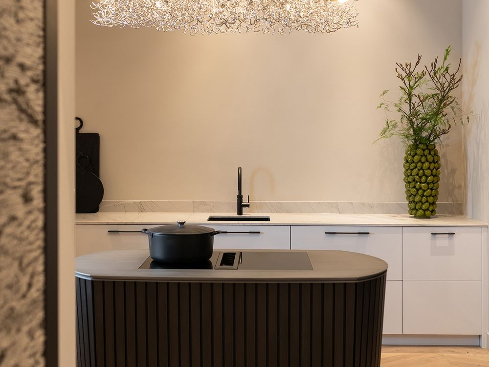 Îlot noir cannelé équipé d’une table BORA sous un lustre de cristal, cuisine d’esprit Art déco