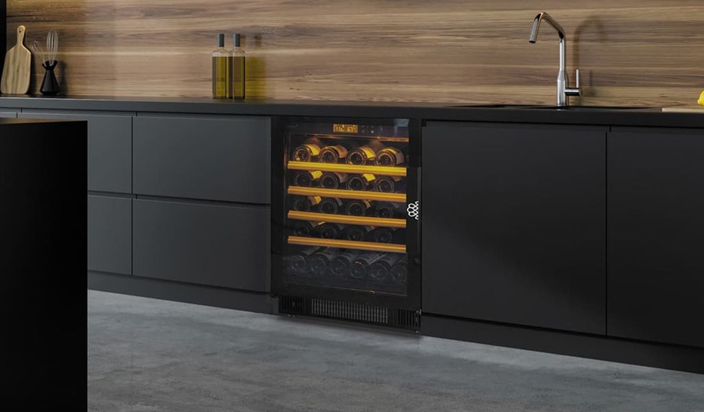 Cave à vin EuroCave Compact sous le plan de travail d’une cuisine noire mate, éclairage ambré