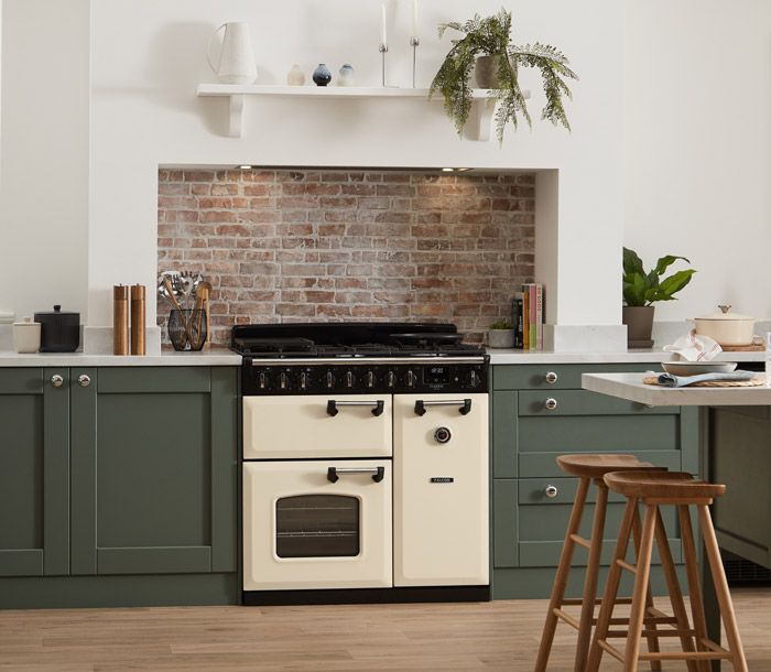 Piano de cuisson Falcon Classic Deluxe 90 crème pastel entre des meubles vert sauge, crédence en briques