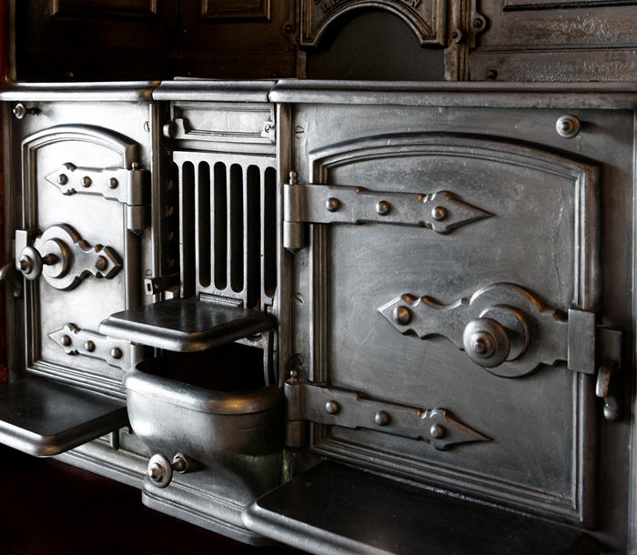 Ancien fourneau de cuisine en fonte ouvragée à portes ferronnées, ancêtre des pianos de cuisson