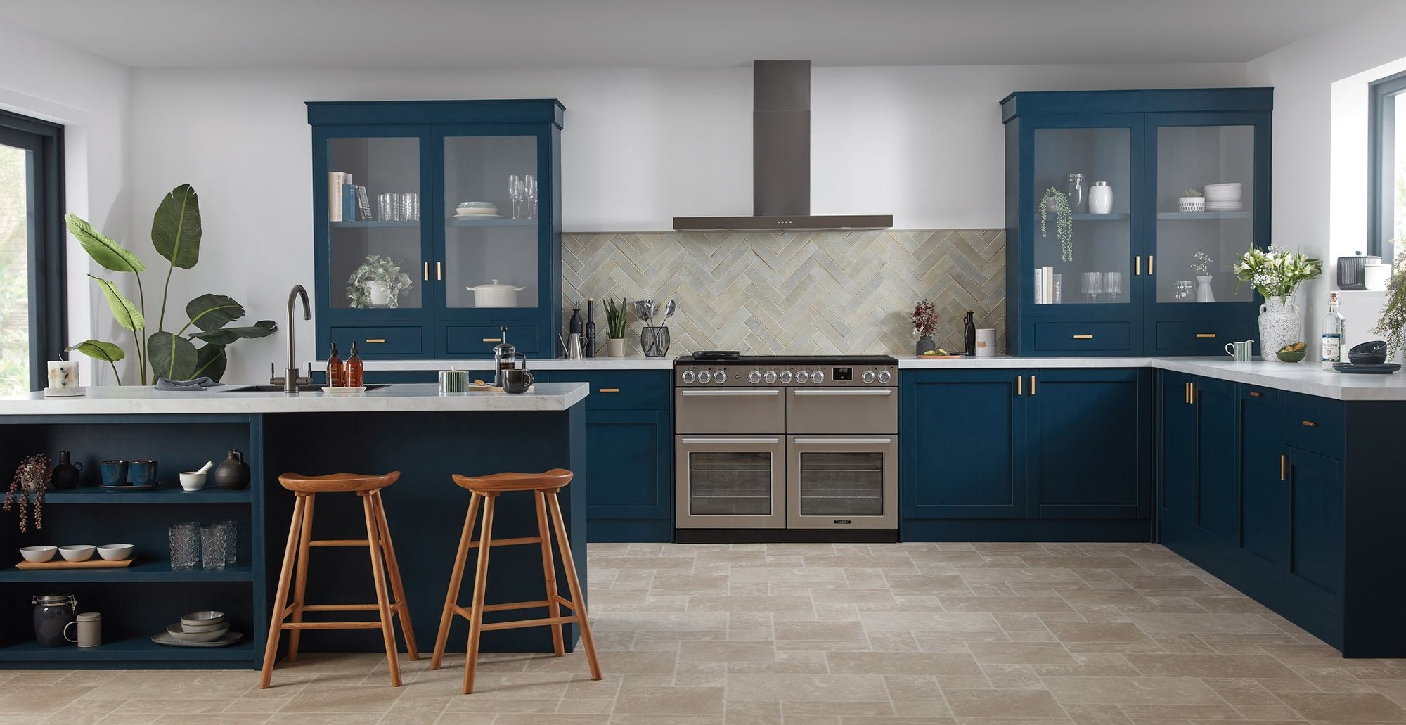 Piano de cuisson Falcon Nexus 110 inox au fond d’une cuisine bleu marine avec îlot et tabourets en bois