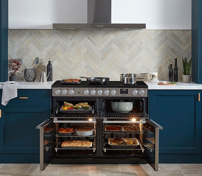 Piano Falcon Nexus 110 inox, fours ouverts garnis de plats, dans une cuisine bleu marine