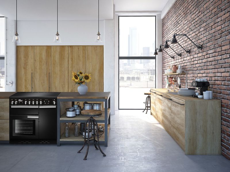 Piano Falcon Professional+ noir à table induction dans une cuisine loft aux murs de briques