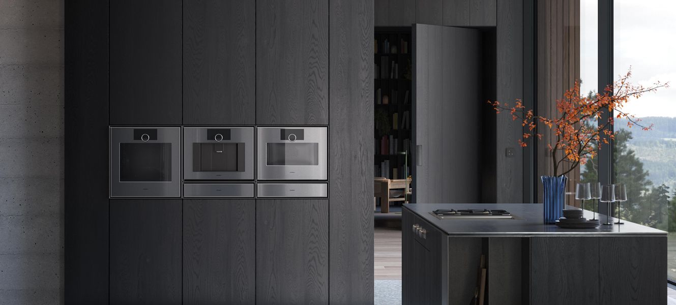 Trois fours Gaggenau série Expressive alignés dans une cuisine en bois sombre