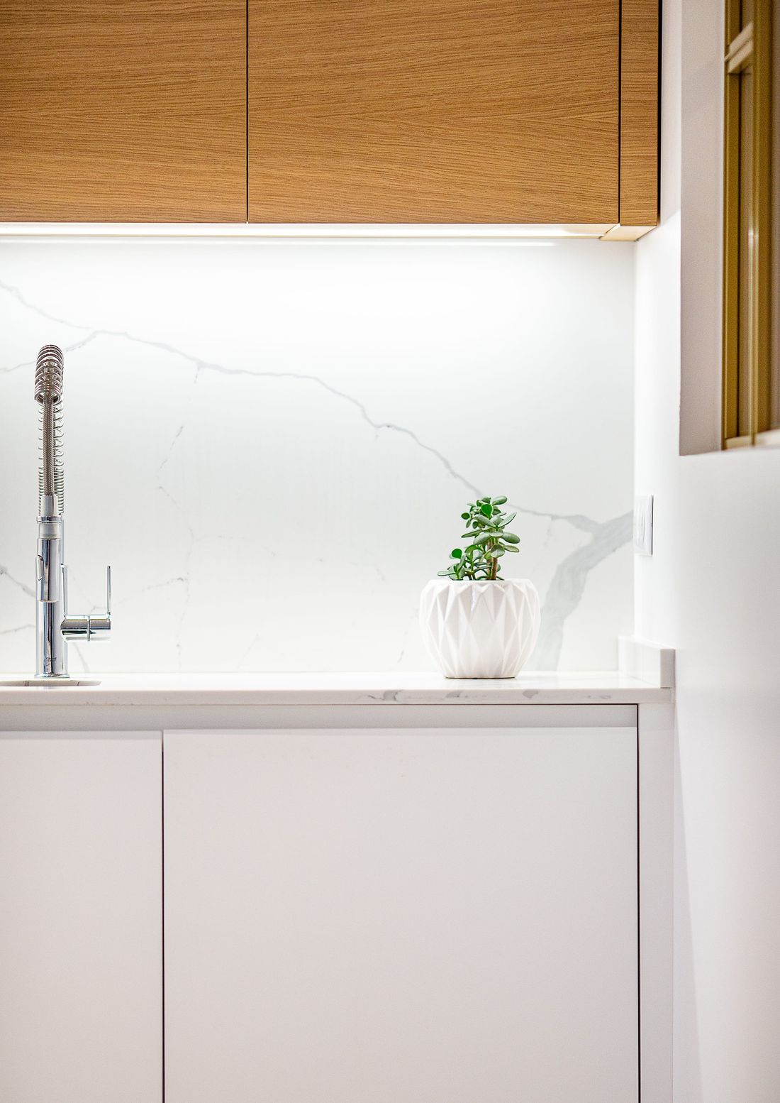 Détail d’une cuisine blanche avec crédence effet marbre et meubles hauts en bois