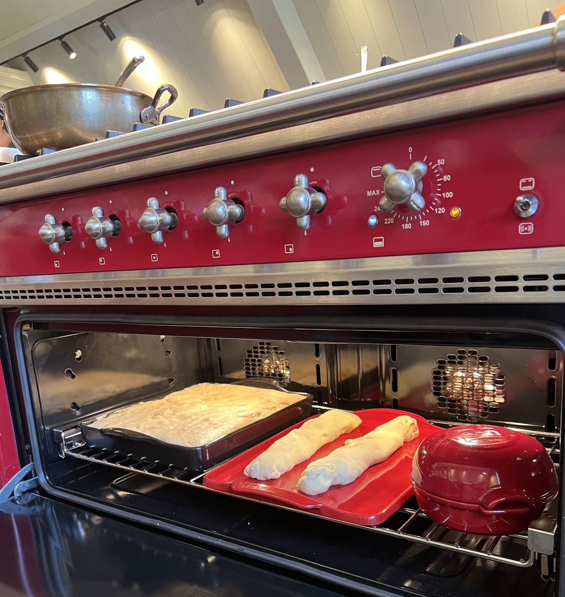 Four ouvert d’un piano Lacanche rouge, plaques de pain et de pâte à cuire, manettes chromées