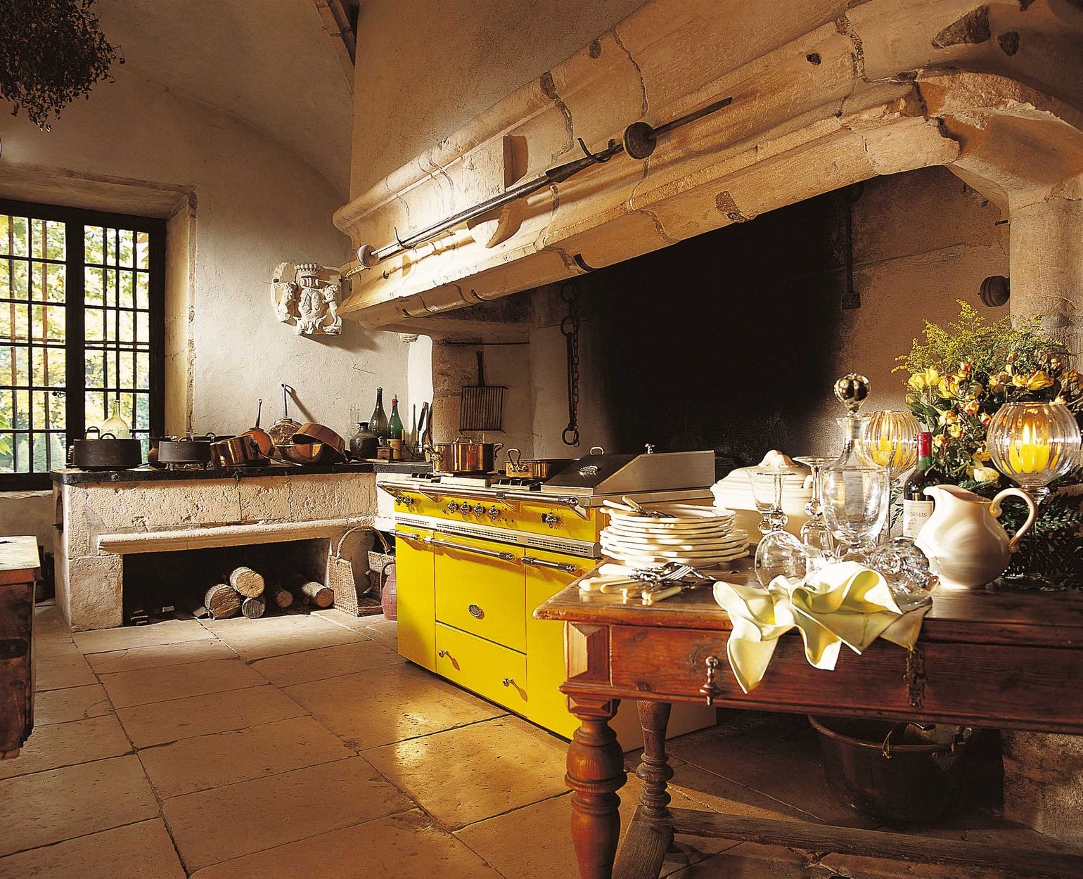 Piano de cuisson Lacanche jaune dans la cuisine voûtée d’un château, devant une grande cheminée de pierre