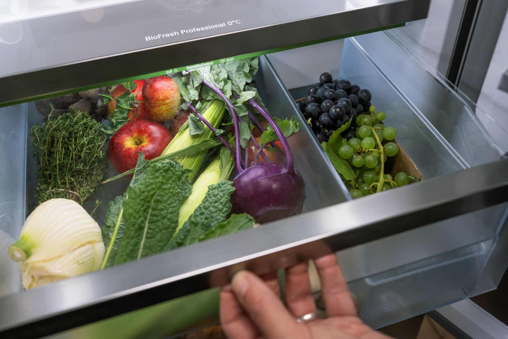Main ouvrant un tiroir BioFresh Professional HydroBreeze rempli de fruits et légumes