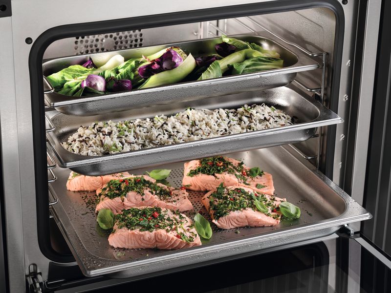 Four vapeur combiné Miele ouvert sur trois plats inox : saumon, riz et légumes
