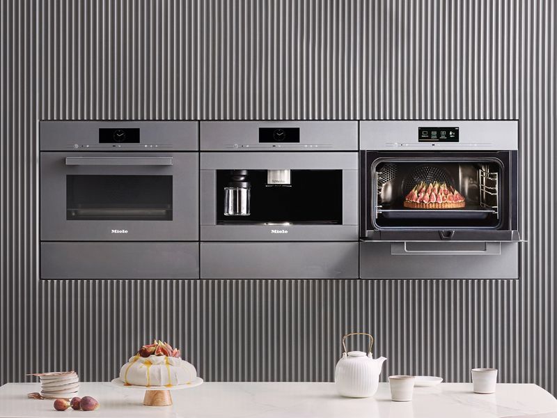 Trois appareils encastrables Miele Génération 7000 gris graphite, dont une machine à café et un four ouvert sur un gâteau