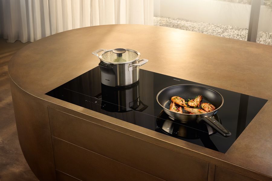 Table à induction Miele KM 8000 et casseroles M Sense sur un îlot arrondi en métal bronze
