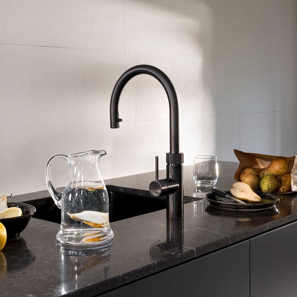 Robinet Quooker Flex Round gunmetal sur un plan de travail noir, carafe d’eau