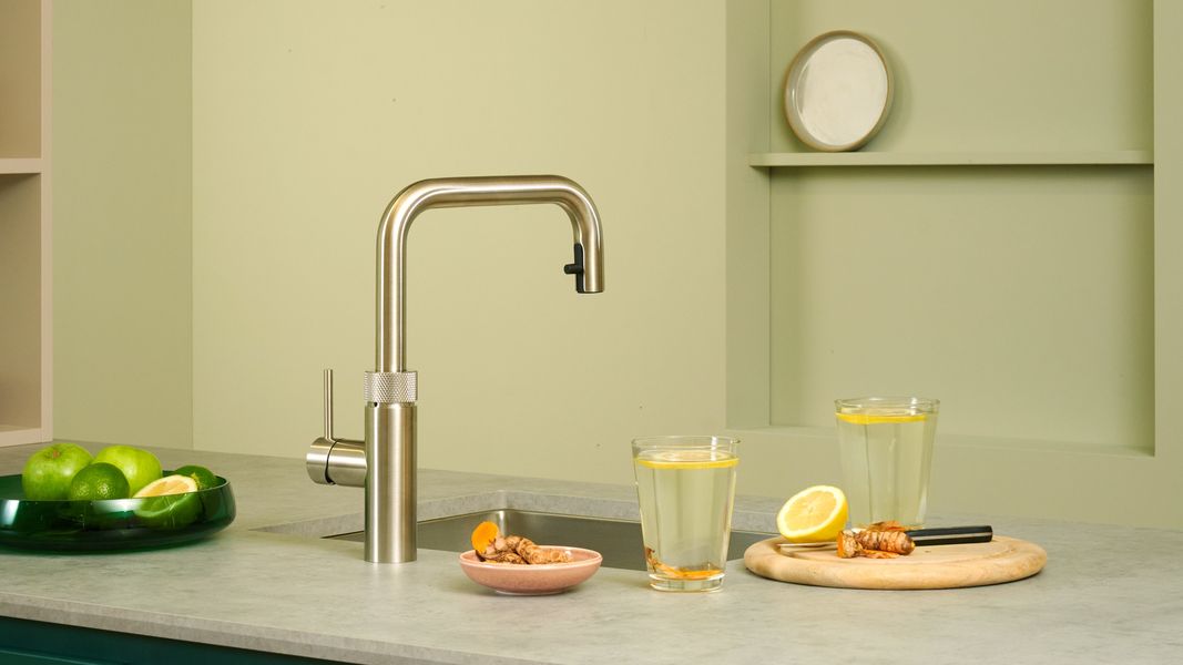 Robinet Quooker Flex Square inox au-dessus d’un évier, verres de citronnade sur un plan vert amande