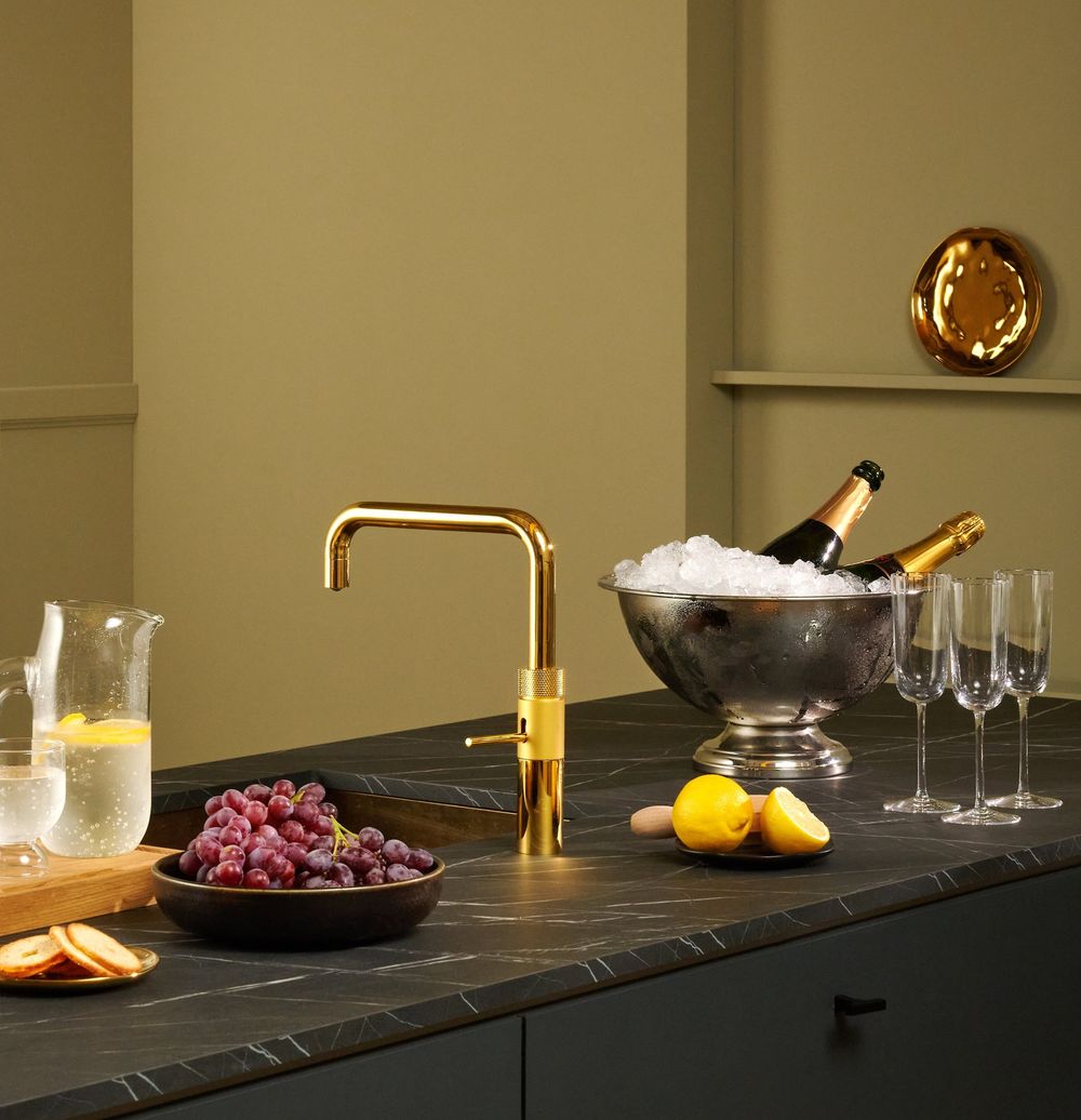 Robinet Quooker Fusion Square doré sur un plan en marbre noir, seau à champagne et flûtes