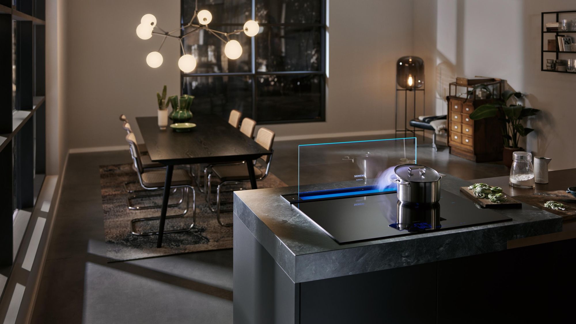 Îlot en pierre sombre avec table induction et hotte de plan de travail Siemens glassdraftAir éclairée, le soir