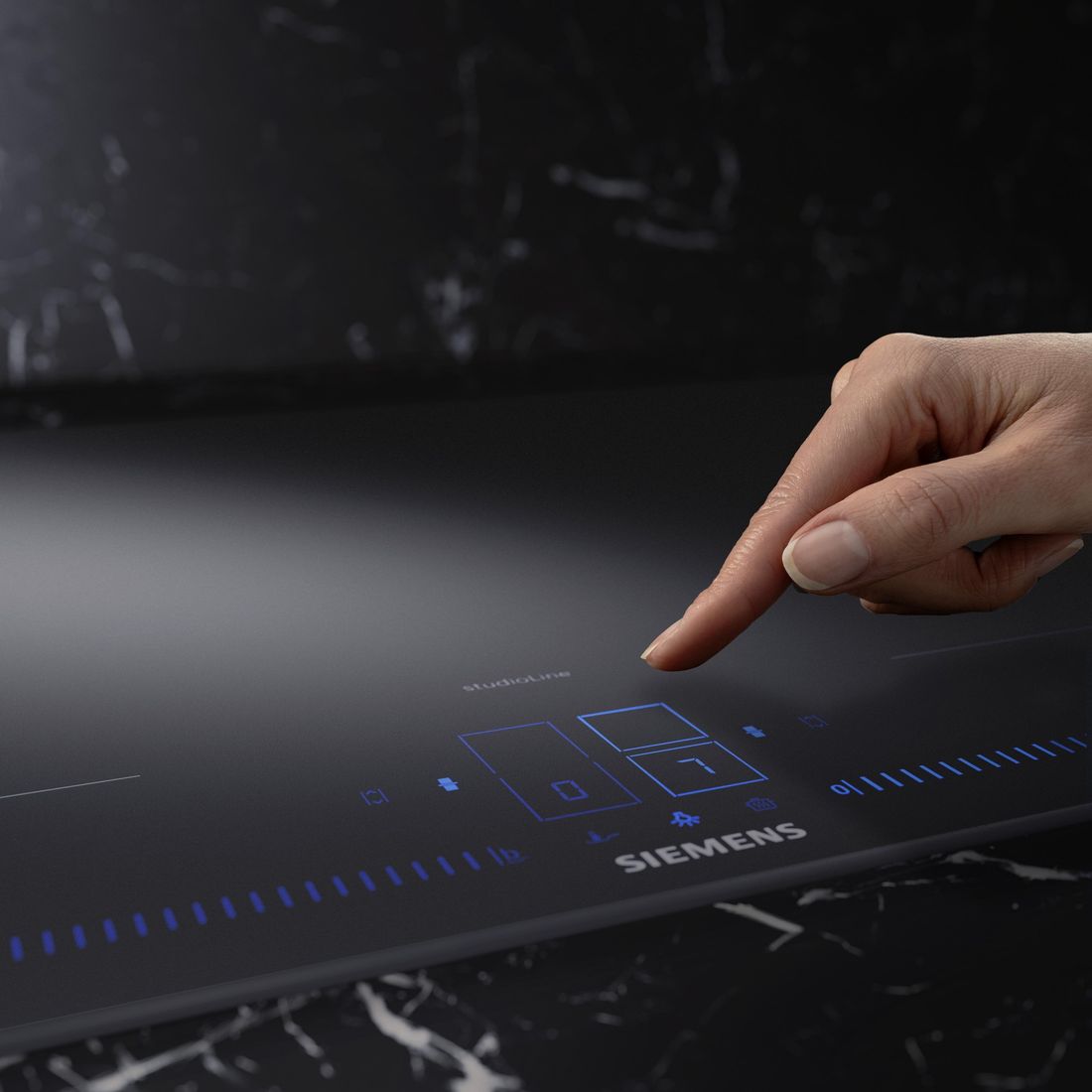 Doigt sur la commande tactile bleue d’une table induction Siemens Matt Edition en verre noir mat